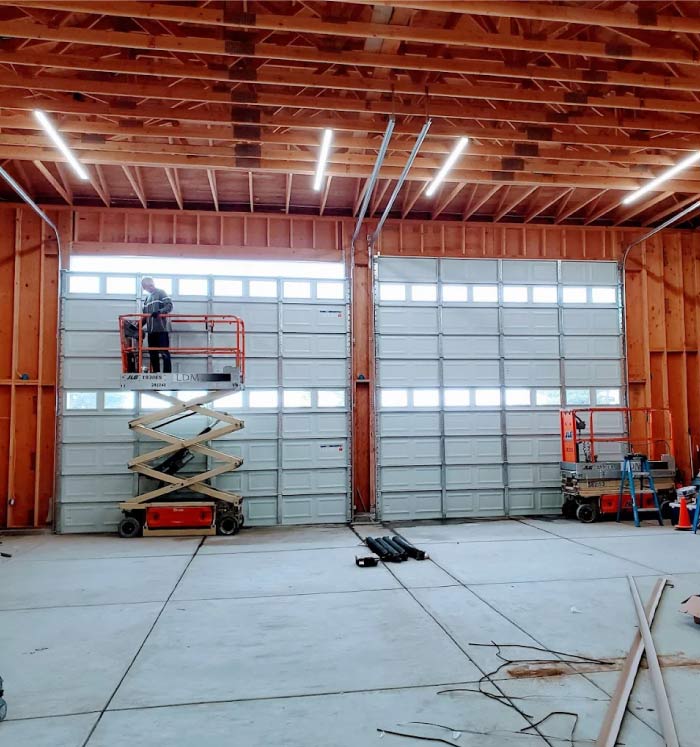 A professional technician on a scissor lift performing high-reach garage door maintenance inside a large commercial warehouse.