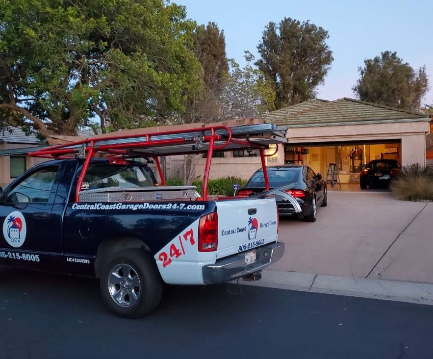 Professional Central Coast Garage Doors 24/7 service truck parked at a residential San Luis Obispo home during a late-afternoon double garage door repair, featuring the company logo, contact number (805-215-8005), and contractor license #1049595.