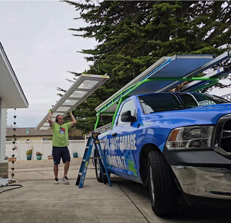 Expert garage door installation being performed by a technician unloading a new door panel from a branded Central Coast Garage Doors 24/7 service truck. The mobile service team serves homeowners and businesses throughout San Luis Obispo County