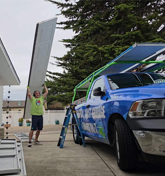 Owner Cory Lewis lifting a large white garage door panel next to a branded Central Coast Garage Doors 24/7 service truck.