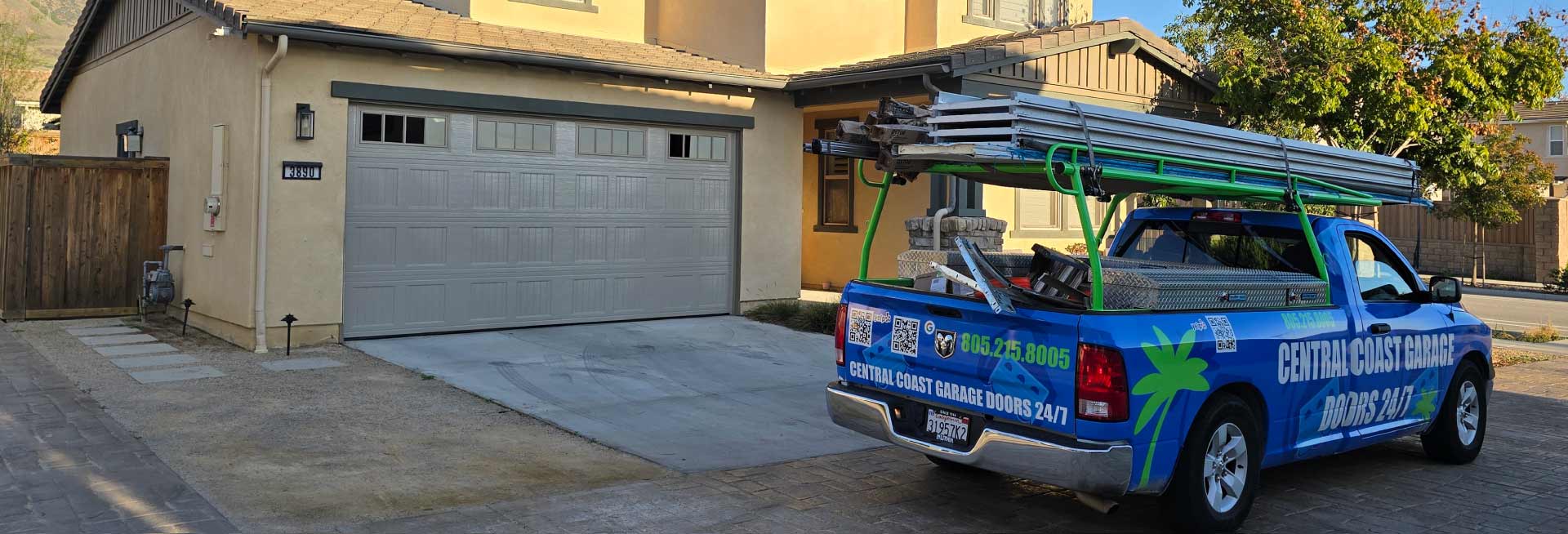 Professional garage door installation in San Luis Obispo featuring a newly installed gray carriage-style door with top-row windows. A Central Coast Garage Doors 24/7 service truck is parked alongside the home, showcasing the mobile repair team's local presence and contact information