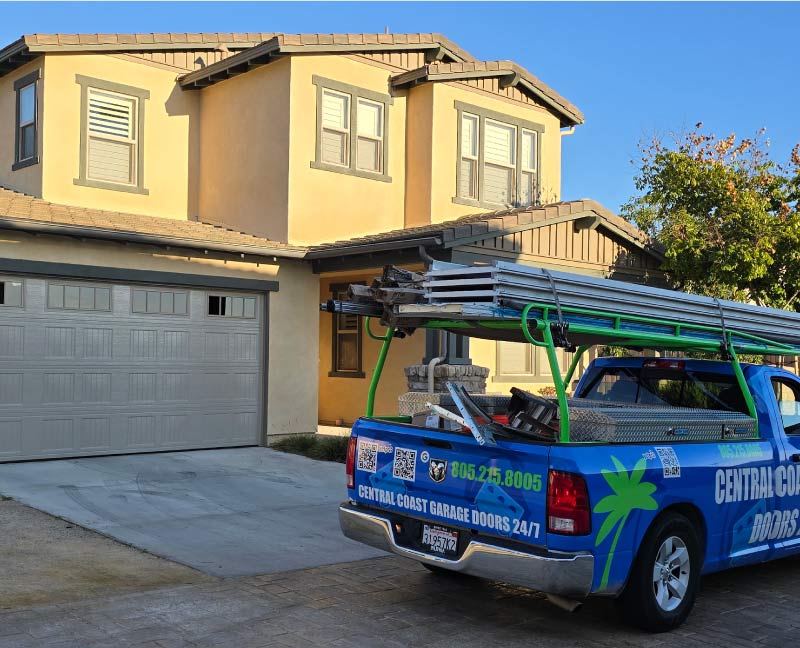 Central Coast Garage Doors 24/7 service truck with a ladder rack and professional equipment parked in a San Luis Obispo driveway during a residential double garage door installation, showing the company website and 805-215-8005 phone number.