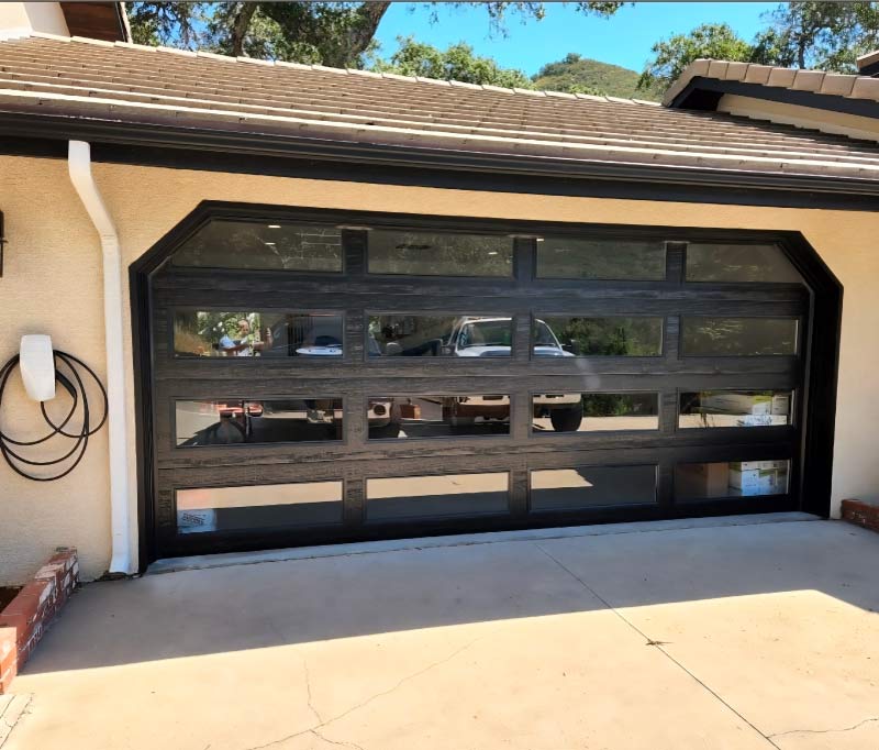 A modern, black-framed glass panel garage door installation on a San Luis Obispo home featuring sleek horizontal windows that reflect the surrounding Central Coast landscape. This contemporary design enhances the property's security and curb appeal.