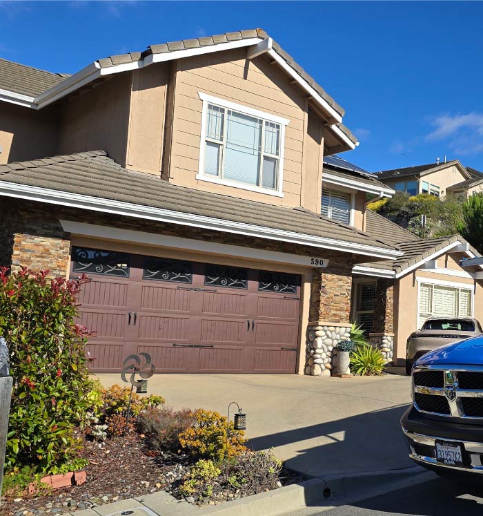 A premium dark brown wood-grain garage door with decorative wrought-iron style window panels on a custom stone-sided house.