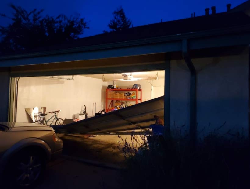 A white residential garage door in San Luis Obispo stuck at an angle due to a broken spring, requiring urgent emergency repair from Central Coast Garage Doors 24/7.