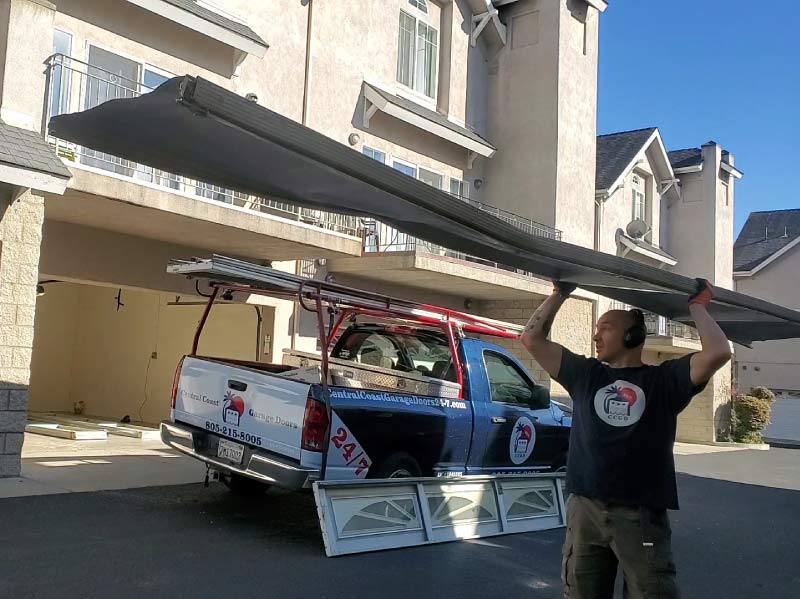 garage-door-technician Central Coast Garage Doors 24/7 owner Cory Lewis lifting a garage door panel next to a company service truck while preparing for a garage door repair in San Luis Obispo.